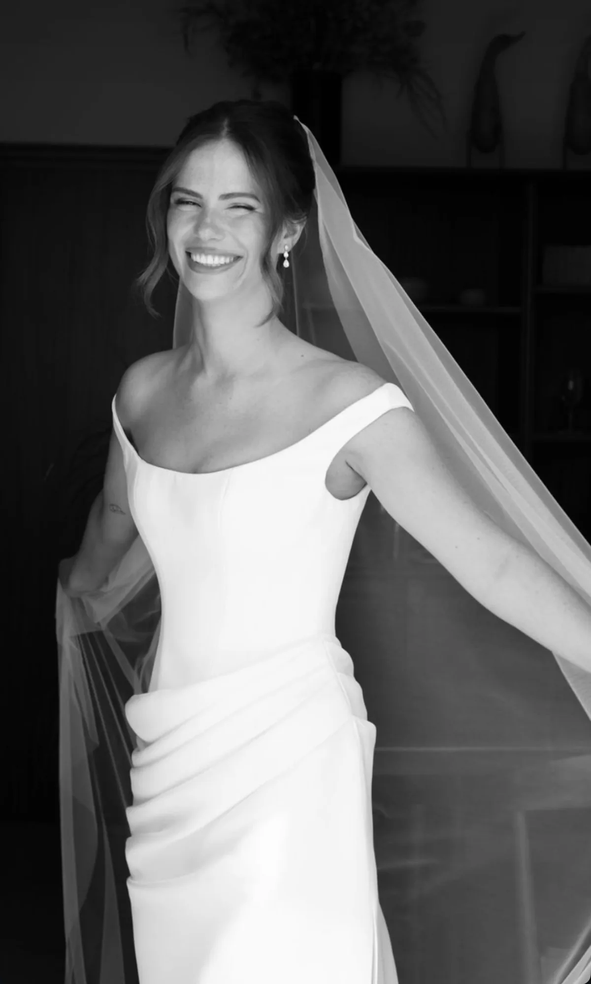 Mariée souriante avec voile, maquillage et coiffure de mariée en noir et blanc